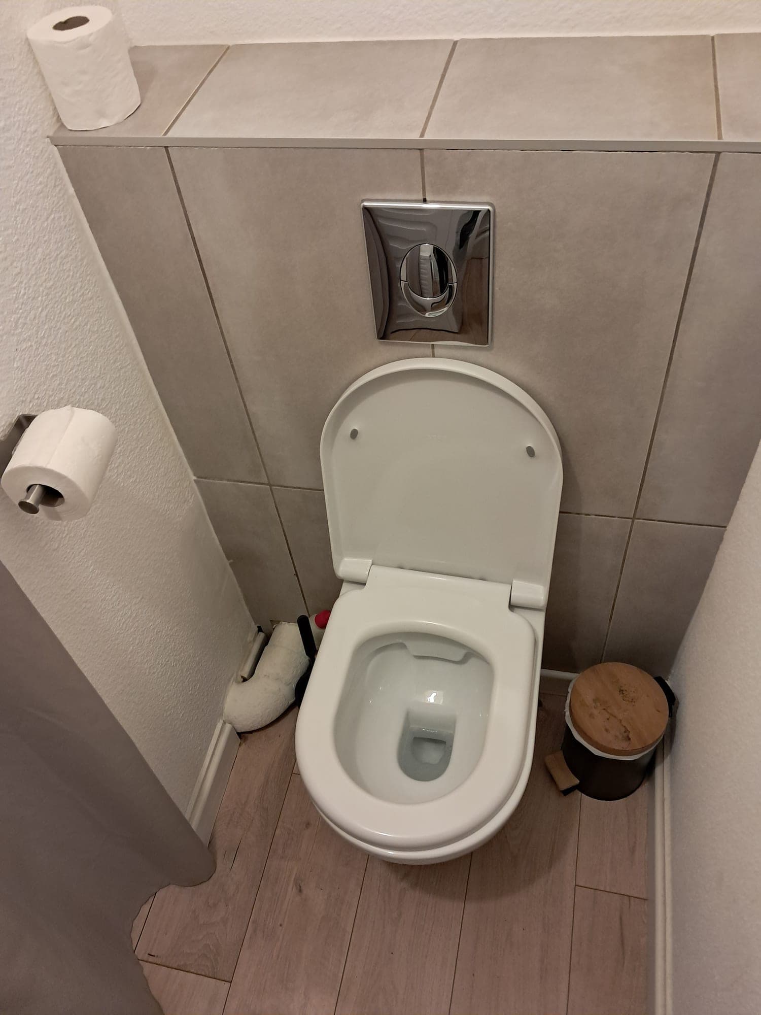 Wall-hung toilet with taupe tiling, disinfected and tidied